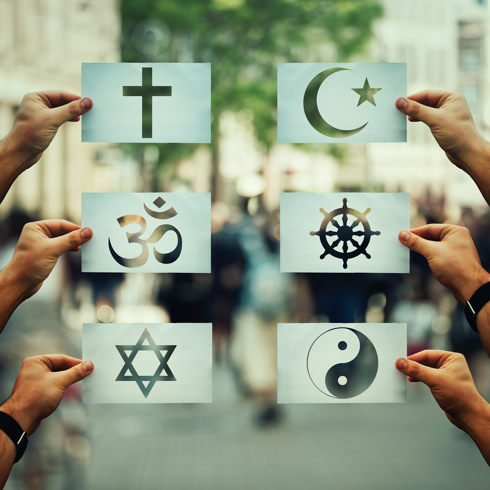 Religion conflicts as global issue concept. Human hands holding different paper with faith symbols over crowded street scene. Relations between different people doctrines and beliefs, social problem.